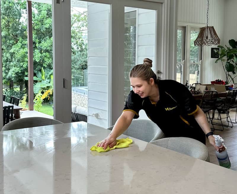 Professional house cleaner smiling while wiping benchtop