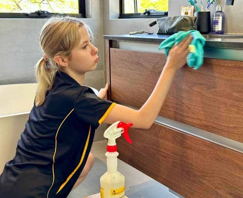 Maid2Match expert cleaner with cleaning supplies cleaning a wooden cabinet