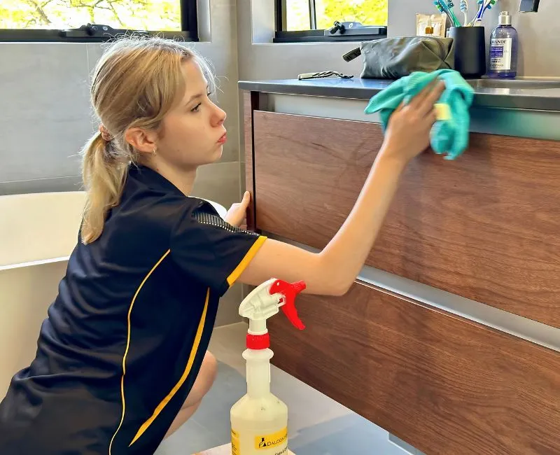 Maid2Match expert cleaner with cleaning supplies cleaning a wooden cabinet